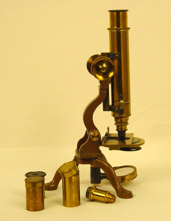 Brass monocular microscope with three legs and extra lenses beside it.